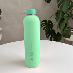 Porter Green driss 1L bottle in Nassau, a mint green matte body with a turquoise cap and metal neck band, on a white table with monstera leaves behind