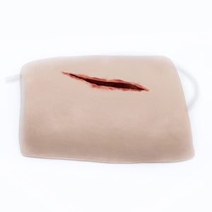 Skin toned moulded training pad with a deep simulated laceration across the centre and a tube outlet at the side