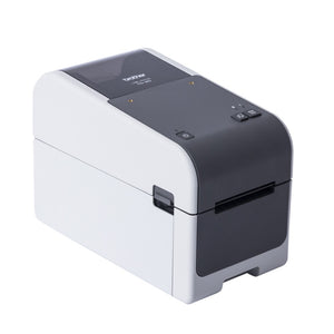 Brother TD-2320D label printer from the front left, white body with a dark grey top panel, power button, two control buttons and three status lights above the label exit slot.