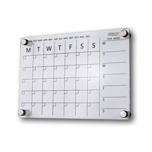 Deflecto A3 acrylic wall planner on a white wall, showing the printed month tick row from January to December, the Monday to Sunday monthly grid and the This Week column, held on four chrome standoff fixings.