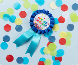 Blue Giggle and Grow birthday badge with a happy birthday message and loose metallic confetti visible inside the clear front pocket.