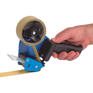 Hand holding a Marbig 87028 packaging tape gun by its black grip, blue frame loaded with brown packing tape feeding past the guarded blade