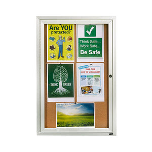 Quartet enclosed cork board shown portrait in an aluminium cabinet, with safety posters, a Think Green tree poster and a green field photograph pinned behind the door and a lock on the right edge