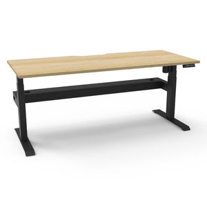 Rapidline Boost Light single sided electric sit-stand desk with a natural oak top on a black frame, a cable tray running under the top, with the controller at the front right edge