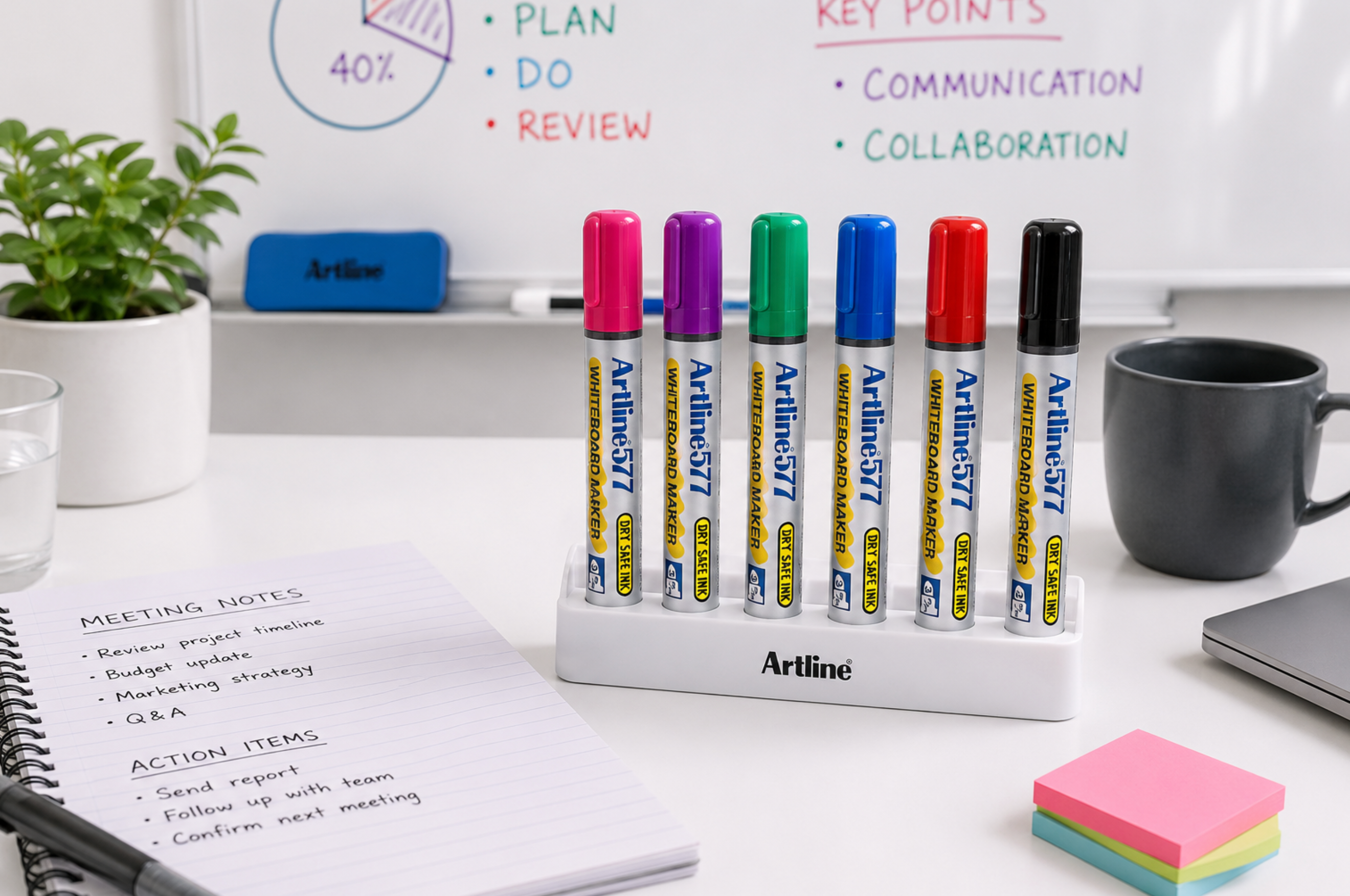 Artline whiteboard marker set in a holder on a bright meeting room desk beside a whiteboard.