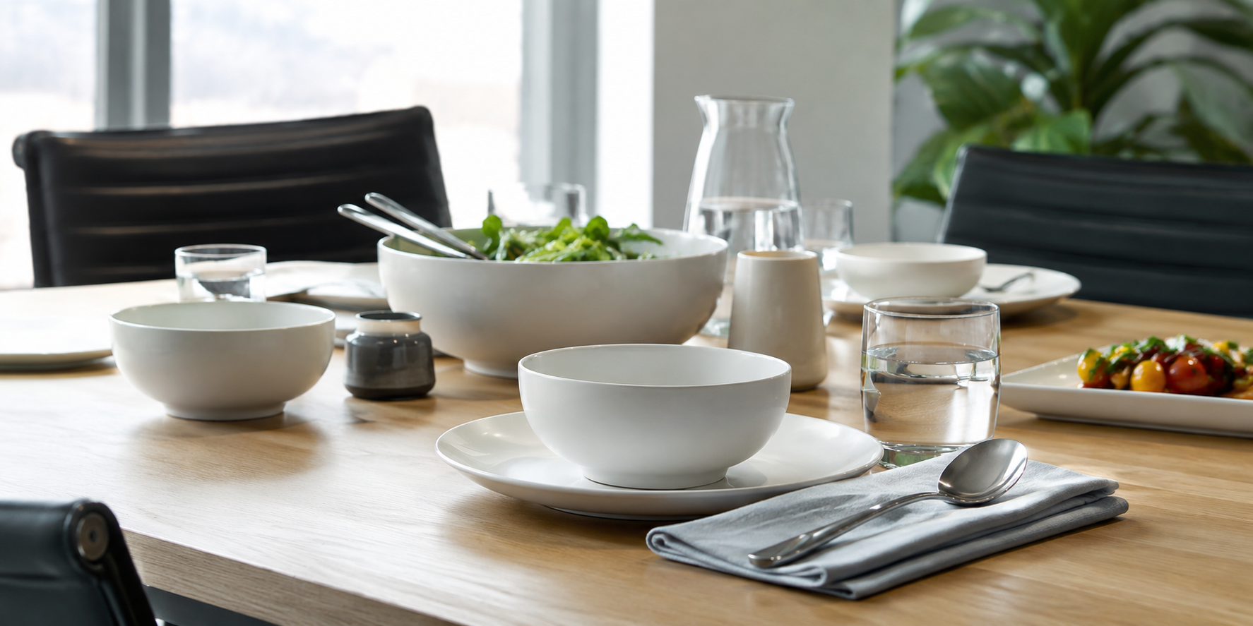 White bowls, plates and glassware arranged on a modern corporate dining or catered meeting table with serving dishes