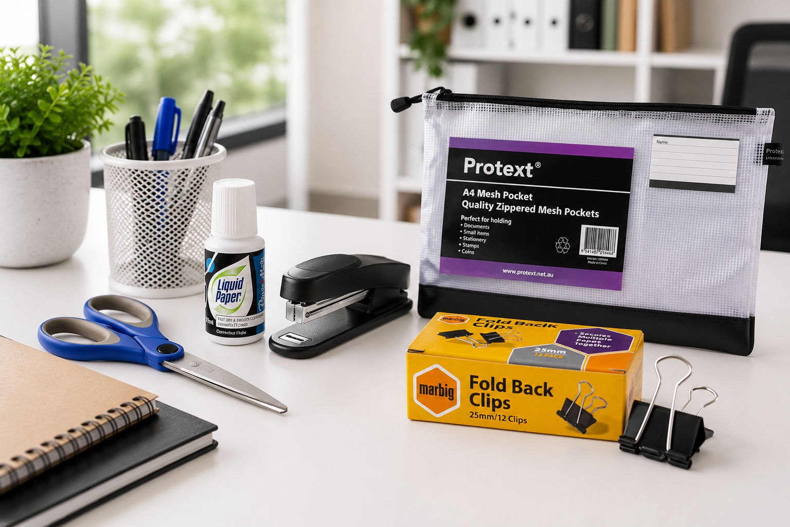 Everyday stationery supplies including scissors, stapler, correction fluid, fold back clips and a mesh document pouch on a bright office desk.