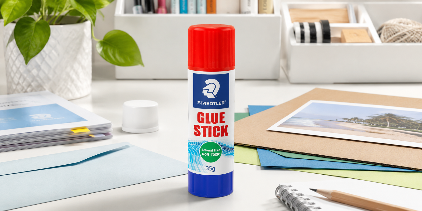 Glue and adhesive products arranged on a bright craft workspace with paper, scissors and office supplies.