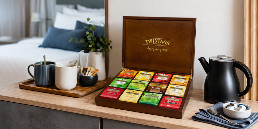 Premium guest tea amenities box with assorted tea sachets, mugs and kettle in a modern hotel room refreshment area