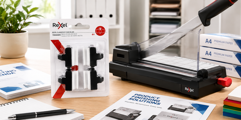 Guillotine replacement blades displayed in a bright print room workspace beside a paper cutter, paper stacks and document finishing supplies.