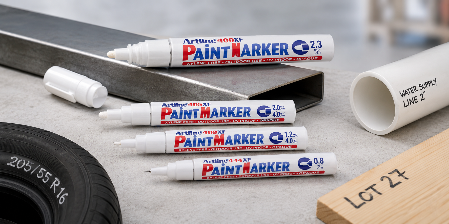 Artline paint markers displayed with metal, timber and PVC materials on a bright workshop bench.