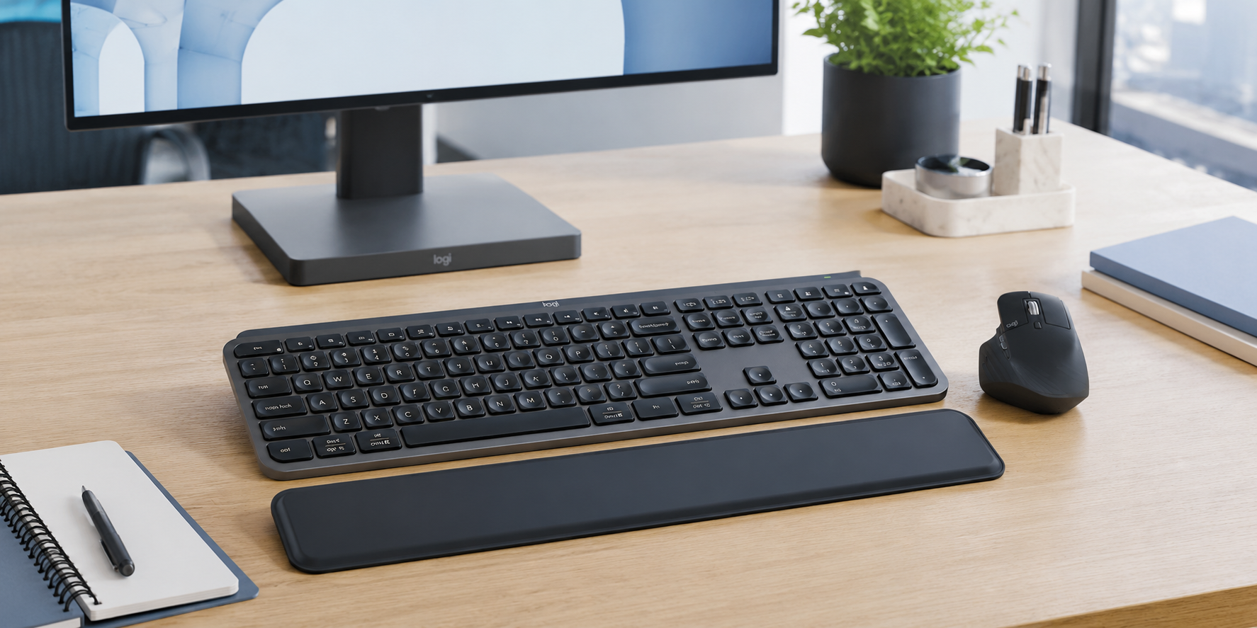 Keyboard and mouse combo arranged on a modern office desk with monitor, wrist rest, notebook and tidy workspace accessories.