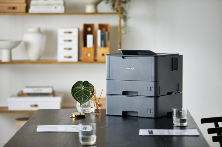 Brother office printer on a modern workstation with documents and organised office storage in the background.