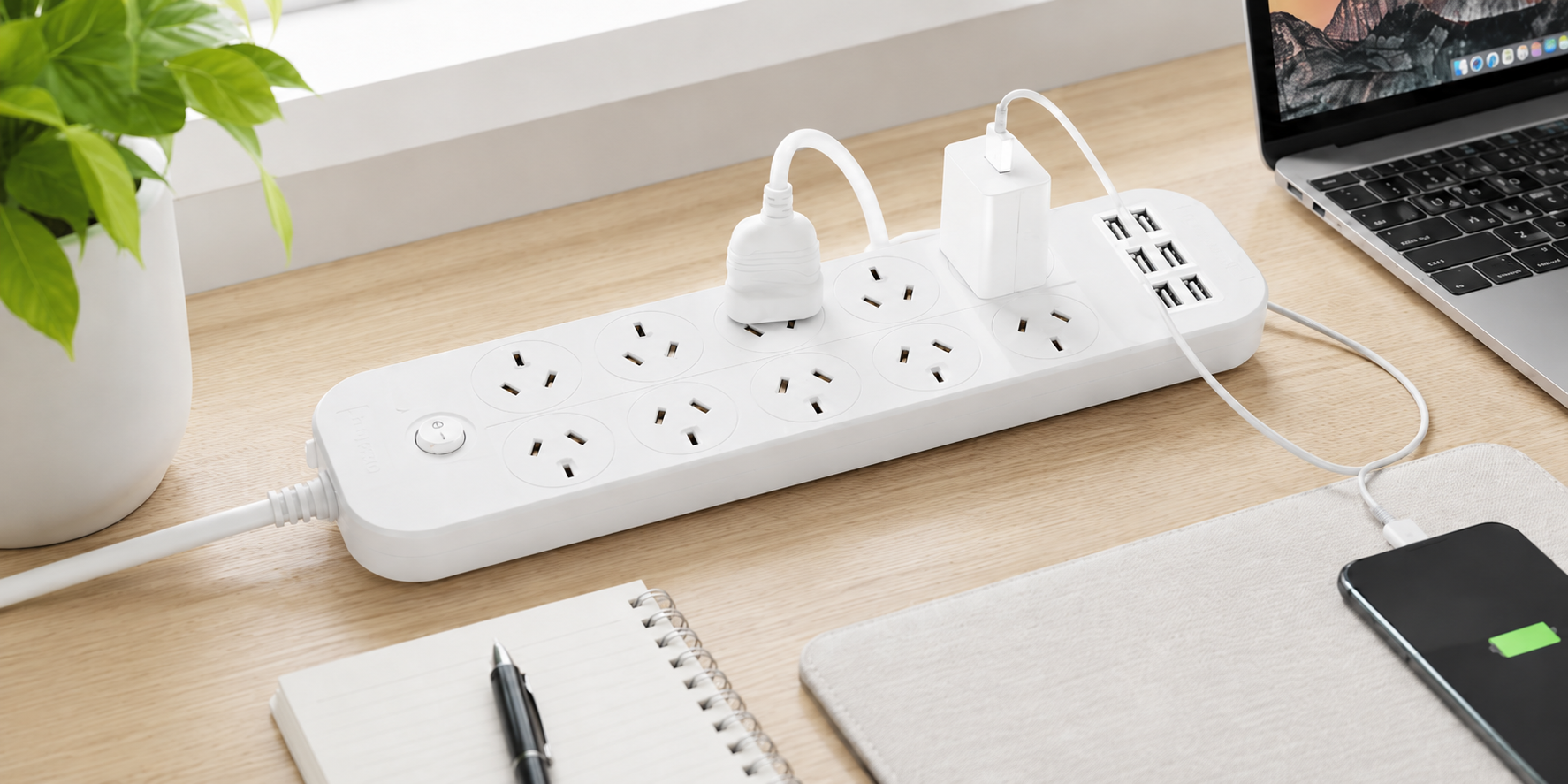 White powerboard charging station on an office desk with laptop, phone, notebook and connected charging cables.