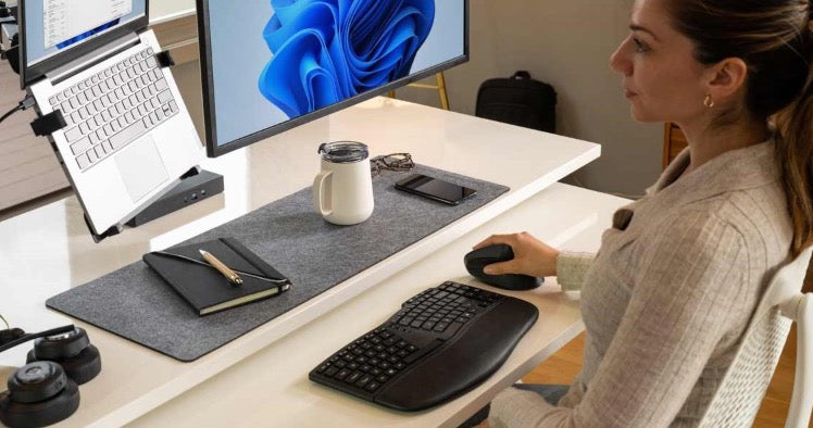Office technology supplies arranged on a modern workstation with laptop stand, monitor, ergonomic keyboard, mouse, dock, headphones and desk accessories.