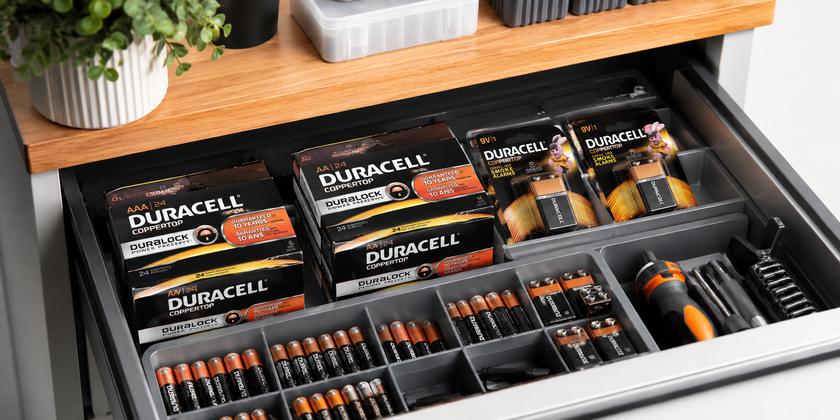 Battery packs and loose batteries organised in a facilities maintenance drawer with small tools and storage compartments in a clean office setup.