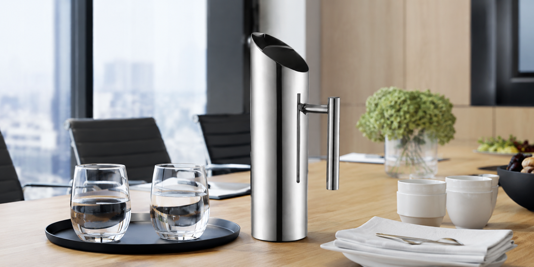 Stainless steel beverage server on a corporate meeting room table with water glasses, cups and catered refreshments