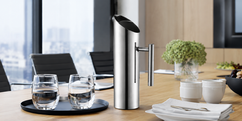 Stainless steel beverage server on a corporate meeting room table with water glasses, cups and catered refreshments