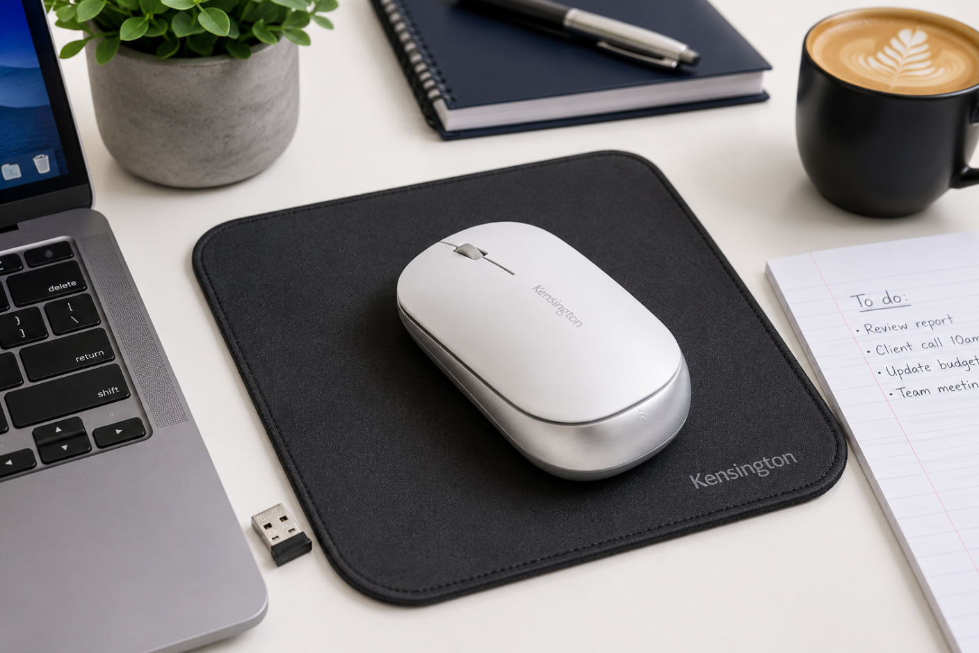 Wireless computer mouse on a mouse pad beside a laptop on a bright modern office desk.