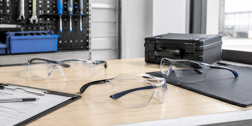 Clear safety glasses arranged on a clean workshop bench with tools and protective storage accessories.