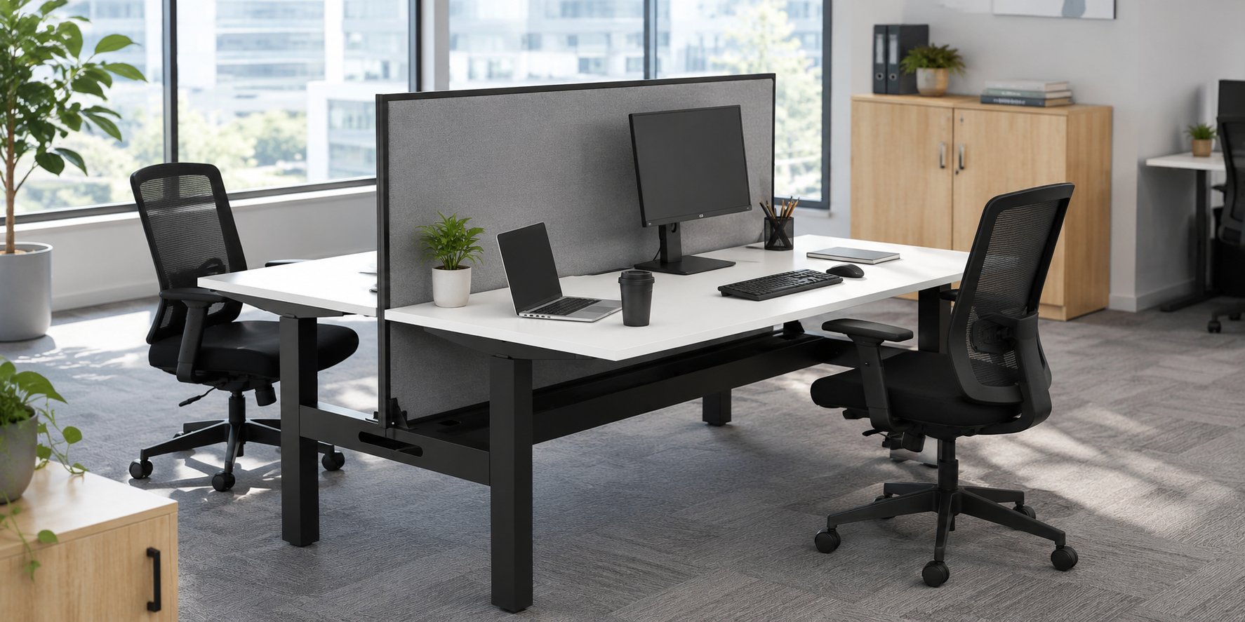 Modern two person office workstation with privacy screen, chairs, laptops and desk accessories in a bright shared office space.