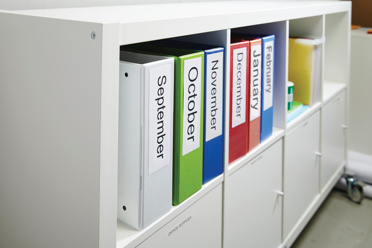 Colorful binders labeled from September to January in a white storage unit.