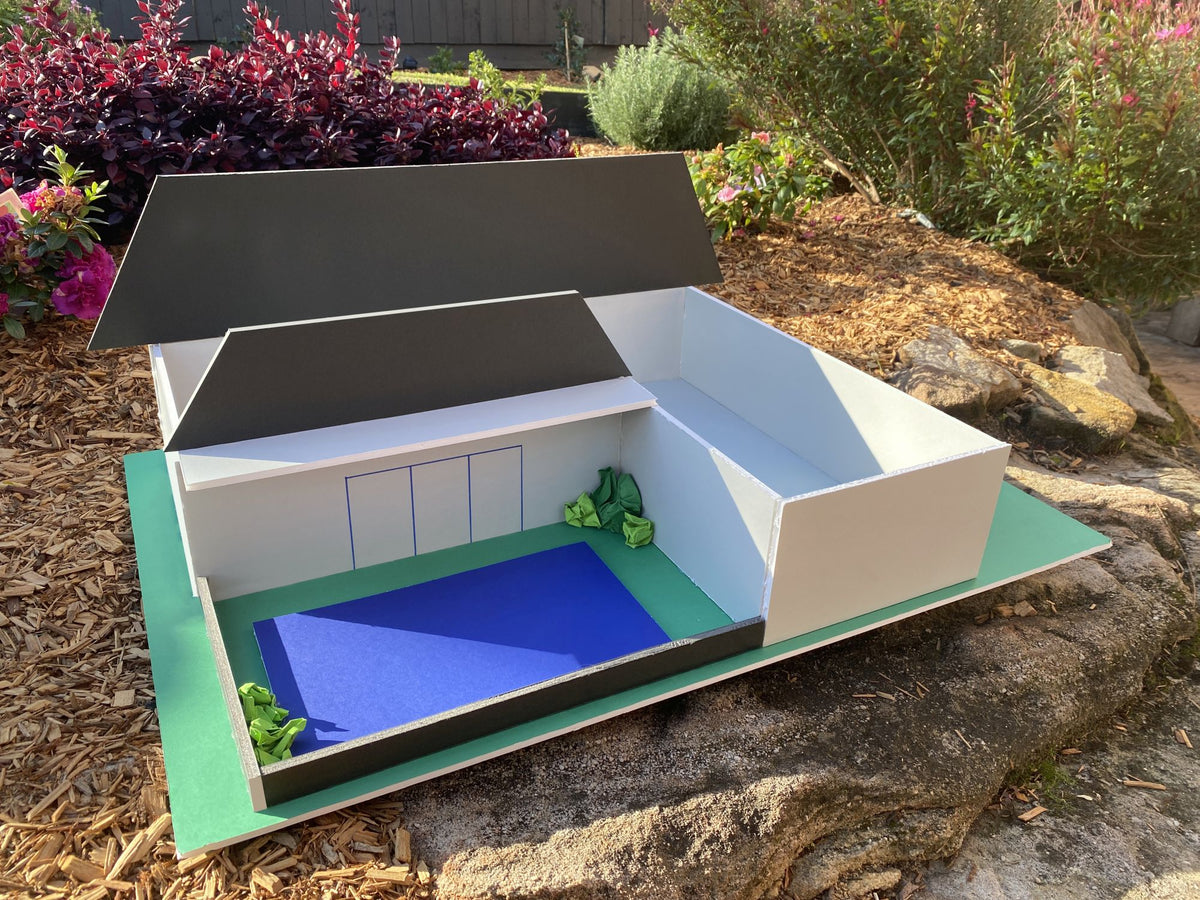 Model house made from white and black foam board on a green base, photographed outdoors on a garden rock as a project example for Quill Foam Board