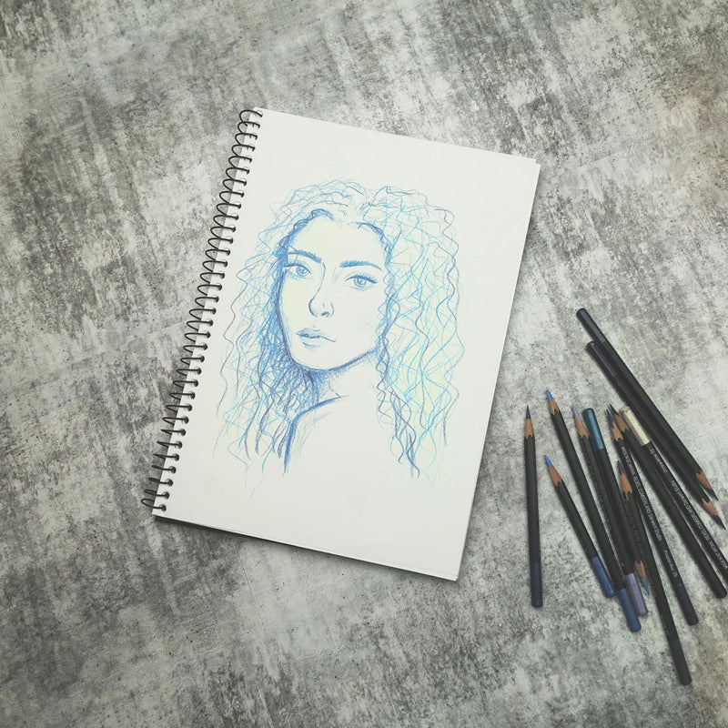 Quill Visual Art Diary A4 open to a blue and green pencil portrait drawing, with a bundle of coloured pencils on a grey surface