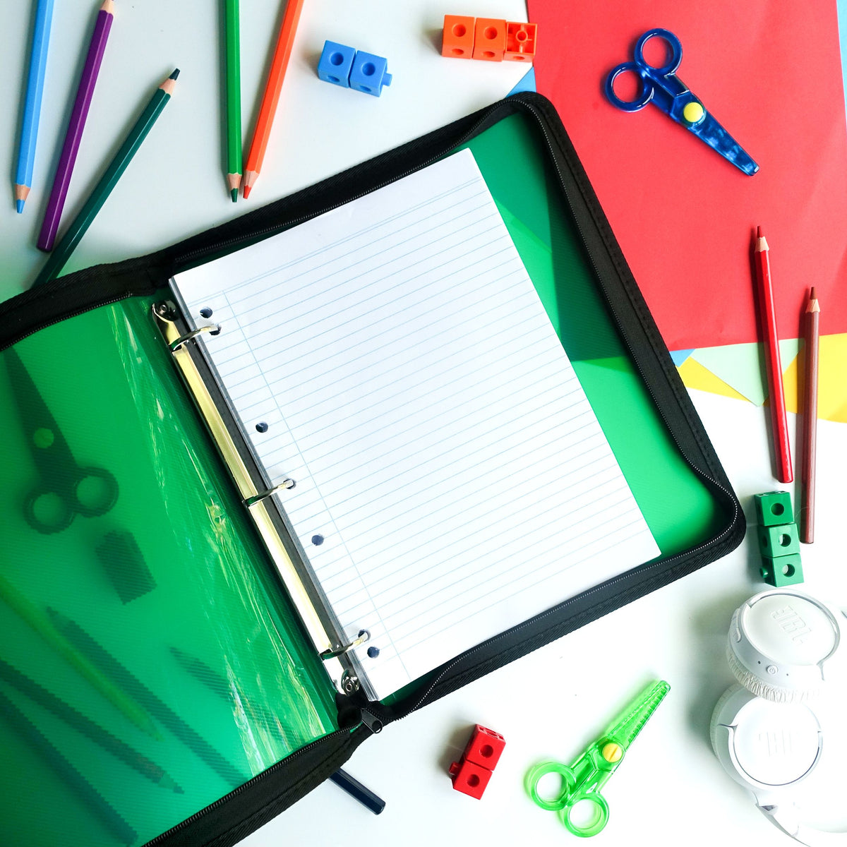 Green Foldermate Pop Gear zipper binder lying open on a desk with ruled A4 refill paper on the three rings, surrounded by coloured pencils, scissors and counting blocks