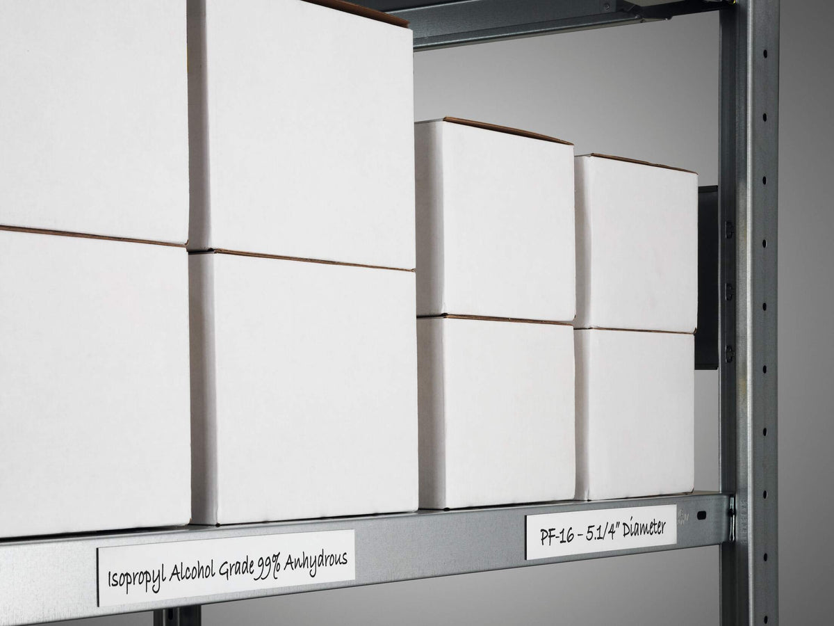 Handwritten white magnetic tape labels along a grey steel shelf with boxes