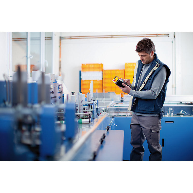 Man in a factory setting using a handheld device.