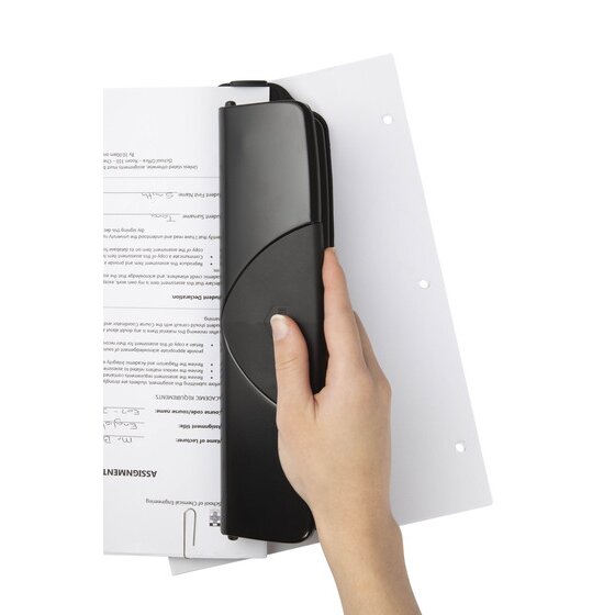 Hand holding a black three hole punch against a sheet of paper, with three punched holes visible along the edge