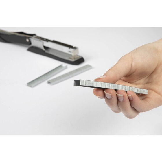 A hand holding a strip of staples in front of an open black stapler, with two loose staple strips on the desk