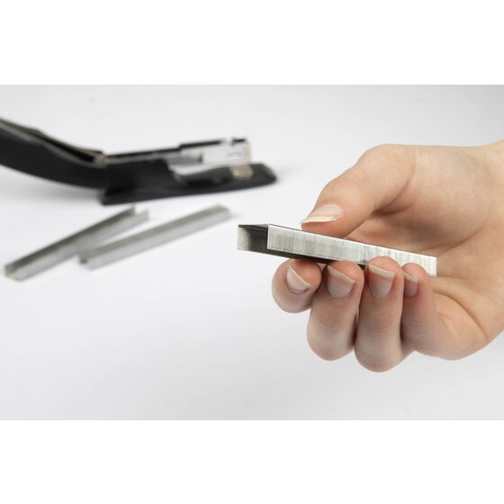 A hand holding a strip of staples beside an open black stapler, with two loose staple strips on the desk
