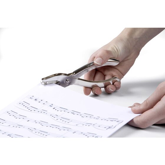 Hand squeezing a silver plier style one hole punch at the edge of a sheet of music