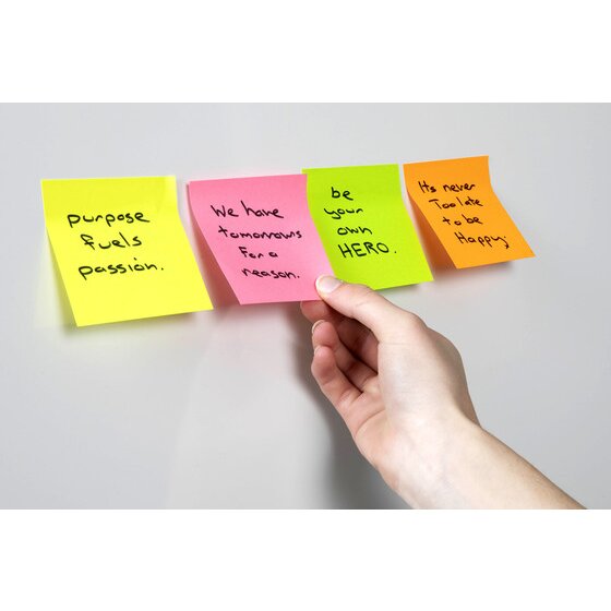 Hand pressing four handwritten notes in yellow, pink, green and orange onto a pale grey wall