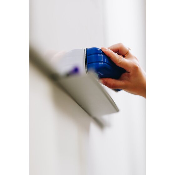 Quartet QTERASER flannel whiteboard eraser in use, a hand holding the blue moulded eraser against a white board with a purple marker in the tray below