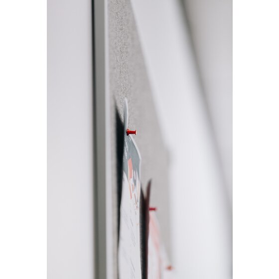 Close side view along the edge of a grey Quartet Penrite felt pinboard, with red push pins holding papers to the felt and the aluminium frame in soft focus