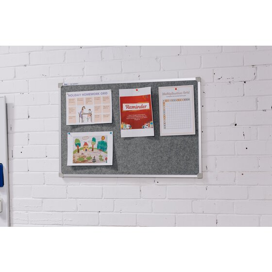 Grey Quartet Penrite felt pinboard mounted landscape on a white brick wall, holding a homework grid, a red reminder notice, a multiplication chart and a drawing with push pins