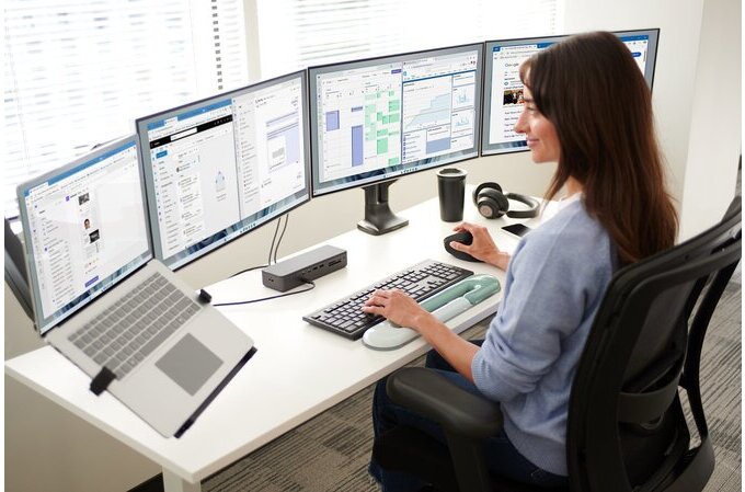 Person working at a desk with multiple computer monitors and a laptop.