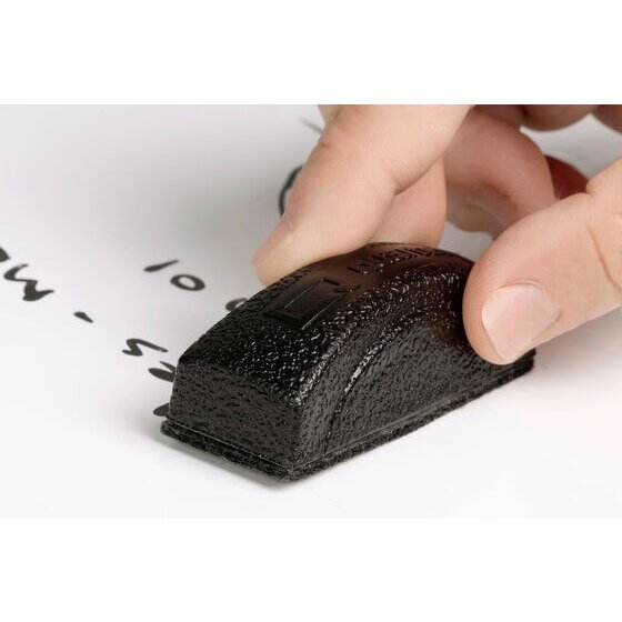 Quartet QTMINIERASER mini magnetic eraser in use, fingers holding a black eraser with a textured top over black handwriting on a white board. 1 eraser is shown, not the pack of 12