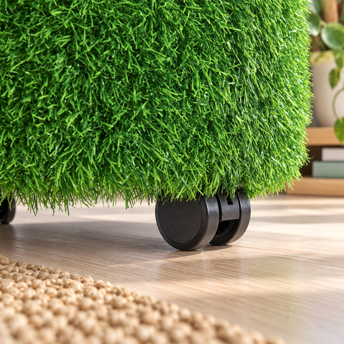 Close up view of the MTA Essentials Aalto Grass Ottoman highlighting the dense green artificial grass texture and a black castor beneath the upholstered base. The detailed image demonstrates the tactile surface and mobile construction, with the ottoman positioned on a timber floor in a warm indoor learning environment.