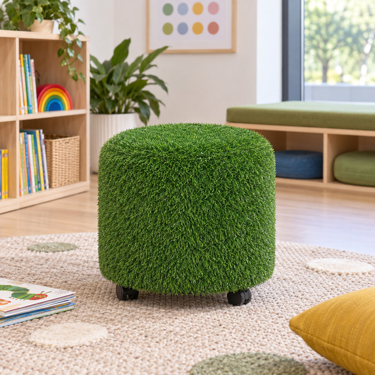 MTA Essentials Aalto Round Grass Ottoman positioned independently in a bright classroom reading area. The 45cm diameter green ottoman features rounded padded sides, tactile artificial grass upholstery and visible black castors, providing flexible nature inspired seating for libraries, classrooms, collaborative areas and sensory focused learning spaces.