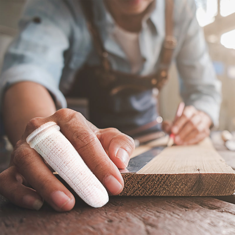 Close view of a person working with timber while wearing an AeroForm tubular finger bandage, demonstrating practical finger protection and support during workshop activities.