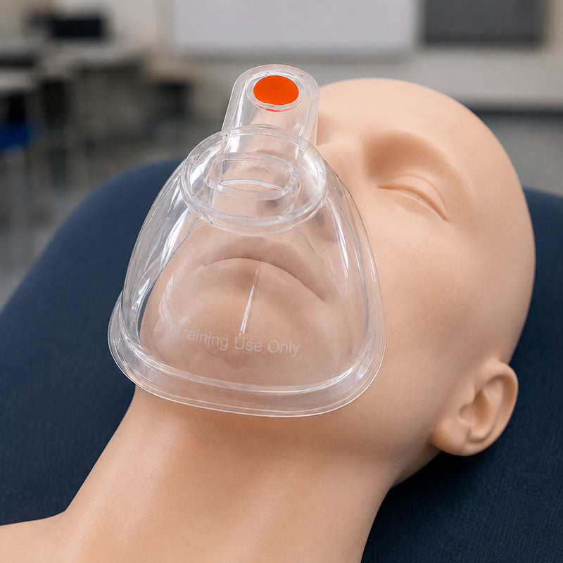 Close view of the AeroLearn Adult Training Mask fitted over an adult manikin face. The clear construction allows the mouth and facial position to remain visible beneath the mask, while the orange identifier and Training Use Only marking help distinguish the equipment as a dedicated respiratory training aid.