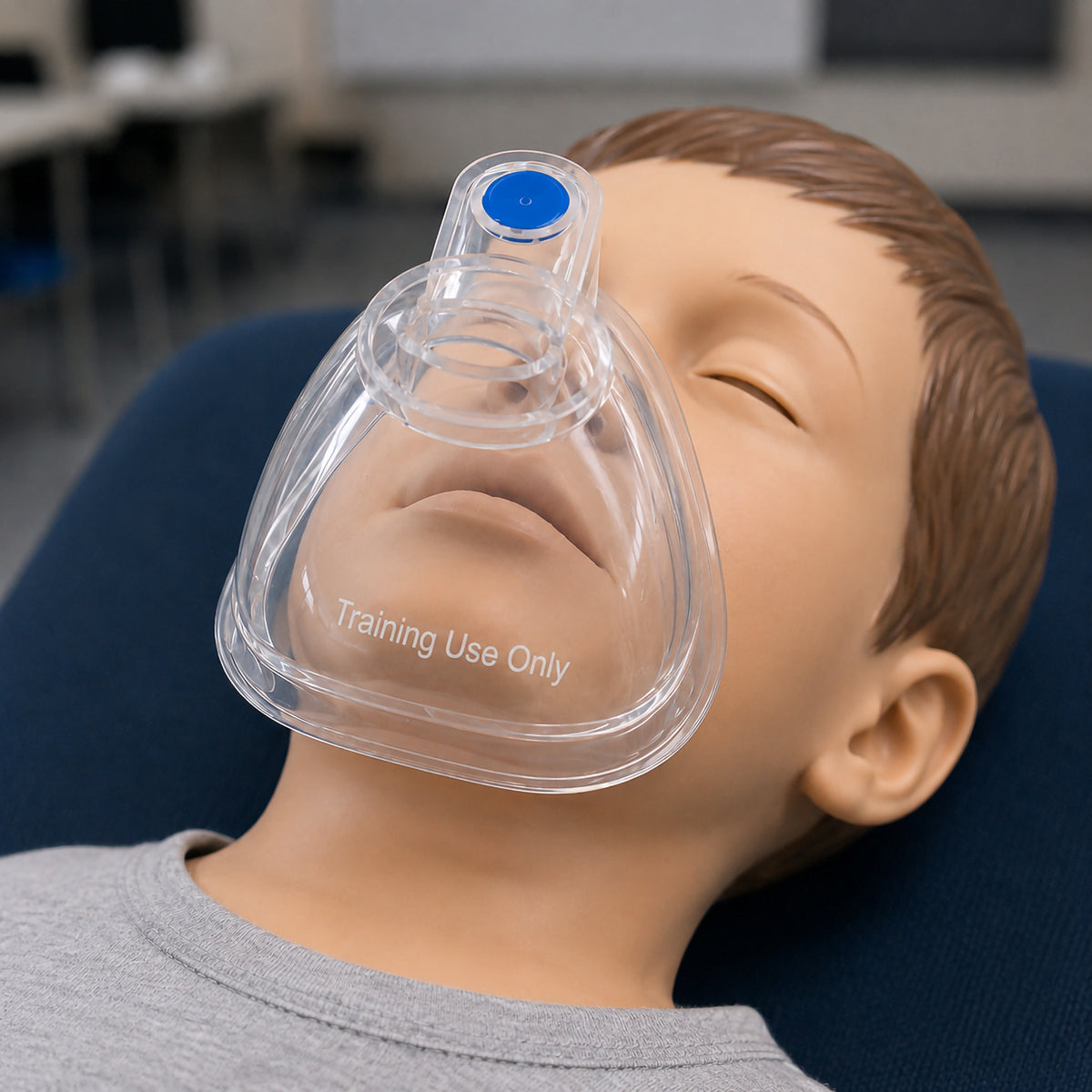 Close view of the AeroLearn Child Training Mask fitted over a child manikin face. The transparent construction allows the nose and mouth area to remain visible, while the blue identifier and Training Use Only marking clearly distinguish the mask as dedicated respiratory education equipment.