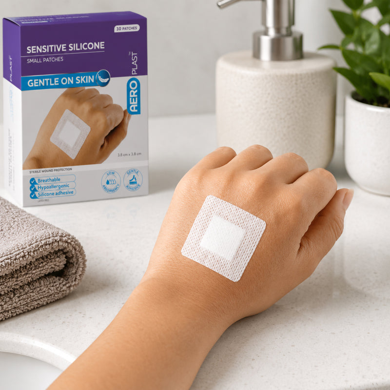 AeroPlast Sensitive Silicone 3.8 x 3.8cm patch worn on a hand beside the product box, demonstrating gentle wound coverage for sensitive skin.