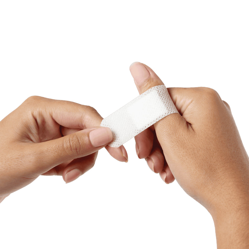 AeroPlast Sensitive Silicone Extra Wide Bandage being wrapped around a thumb against a clean white background, demonstrating the broad flexible strip and conforming fit during application.