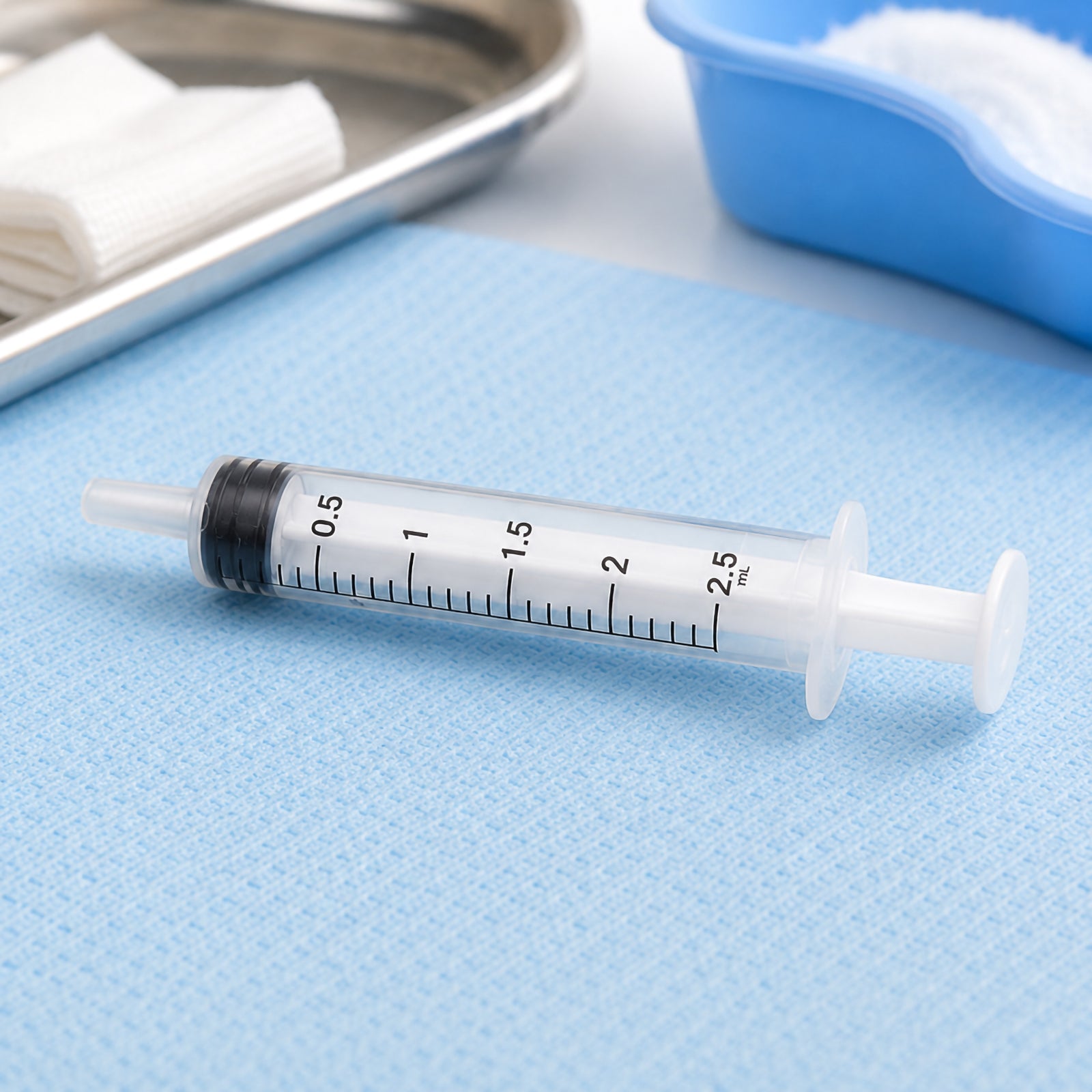AeroSupplies 2.5ml Luer Slip Syringe positioned on a blue clinical drape beside gauze and preparation trays. The transparent barrel and black graduations from 0.5ml to 2.5ml are clearly visible, providing a detailed view of the syringe construction, luer slip tip and plunger.
