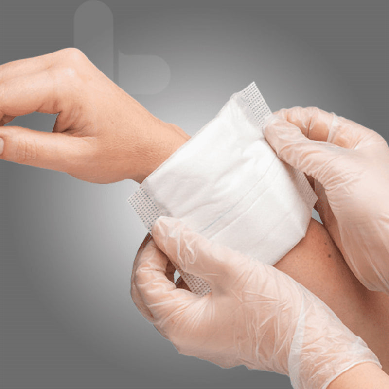 Close clinical application view showing gloved hands positioning a white AeroWound Combine Dressing around a patients wrist and lower arm. The image demonstrates how the soft absorbent pad can sit against the wound area before being secured with an appropriate fixation method for protective wound care.